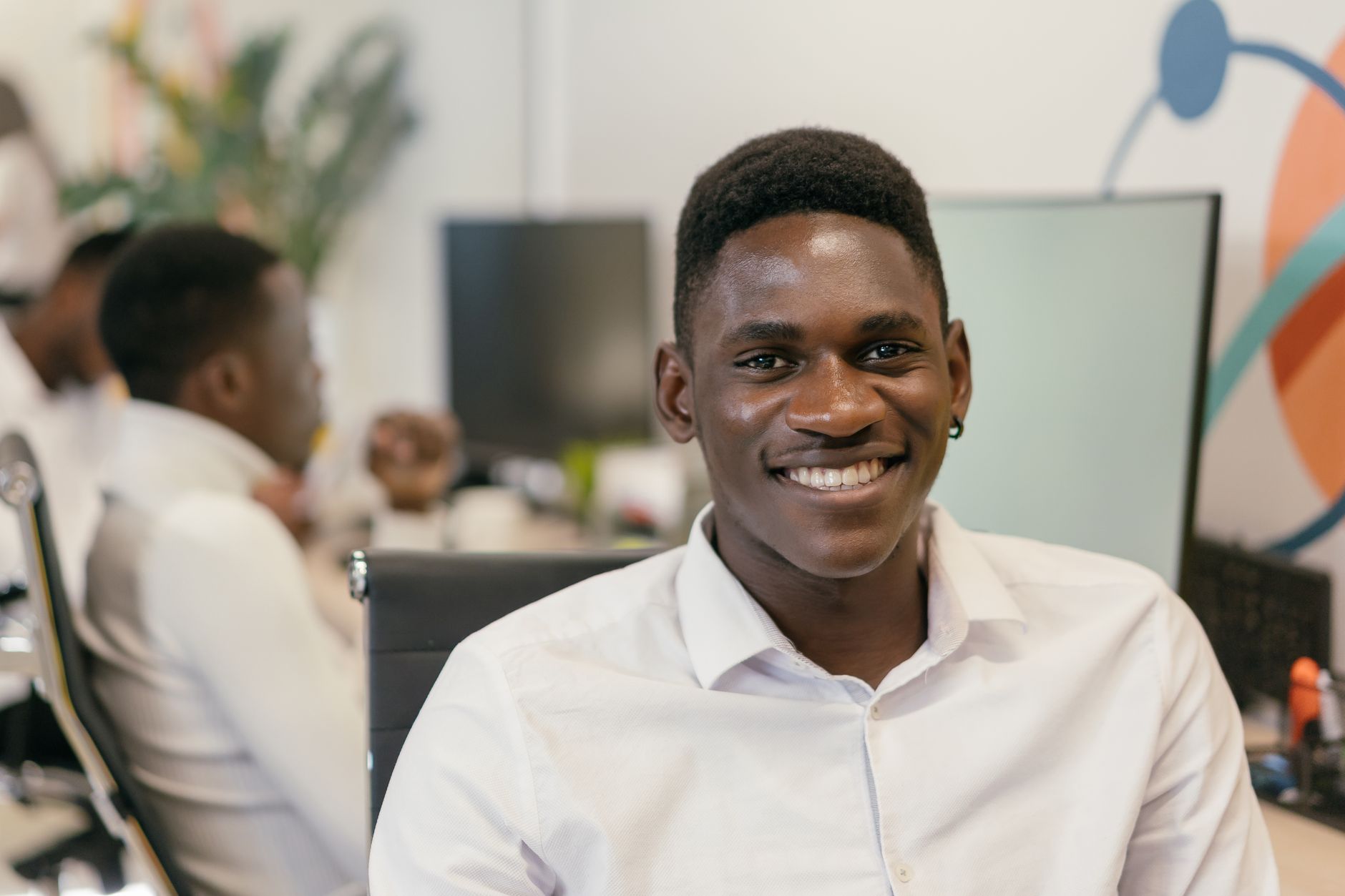 A young professional smiling at his desk in a bright modern office, working through his morning inbox.