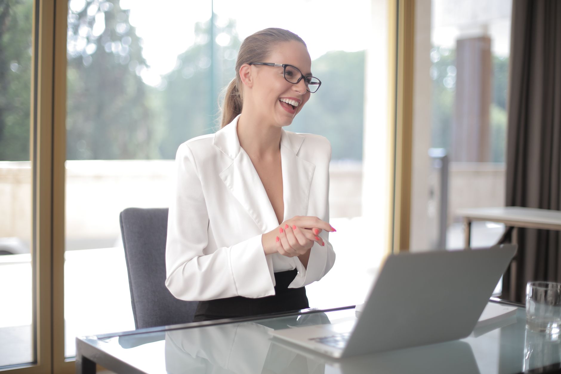 A woman entrepreneur in formal wear reviewing documents and a laptop while working in a modern office.