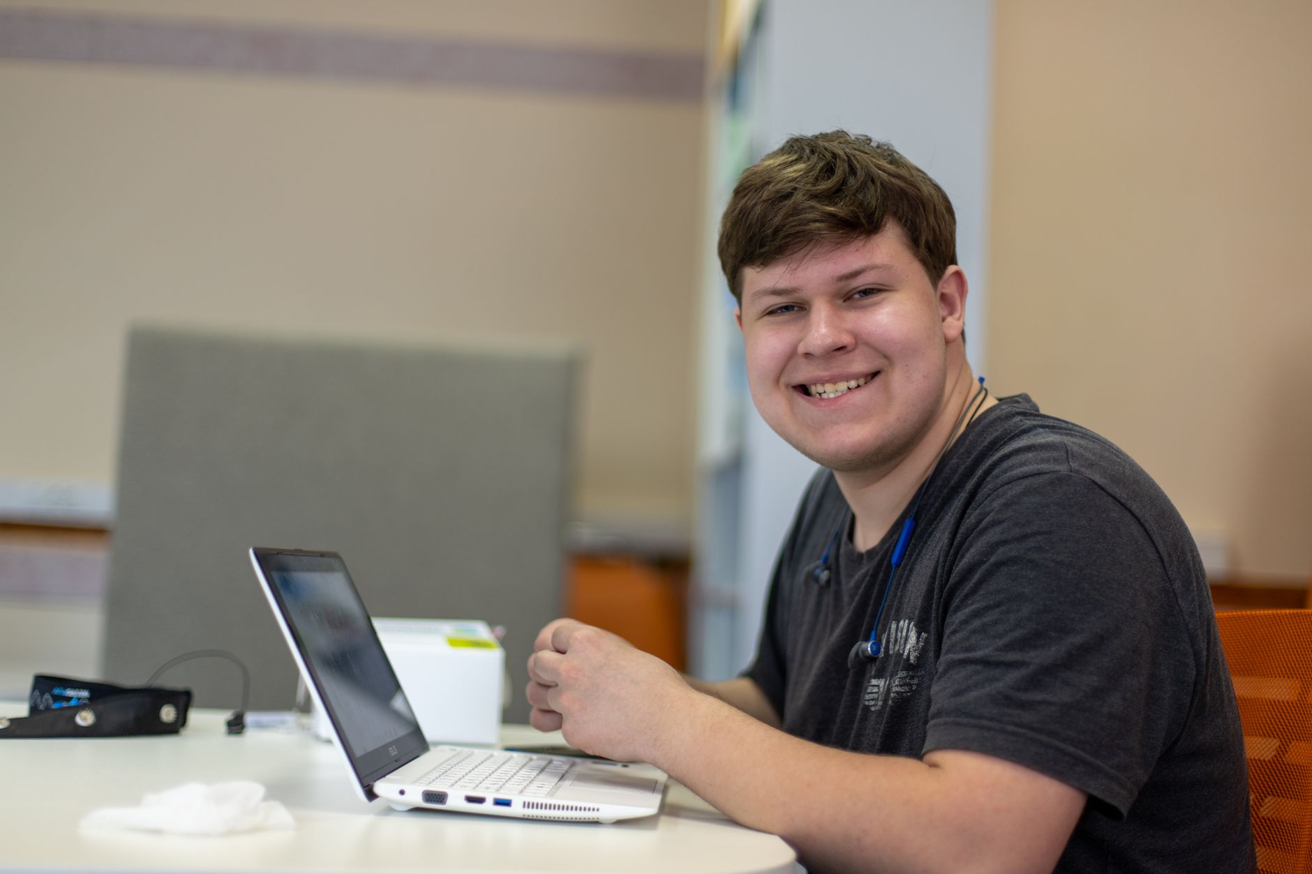 A young man smiling while working on a laptop in a relaxed, modern home-office setting.